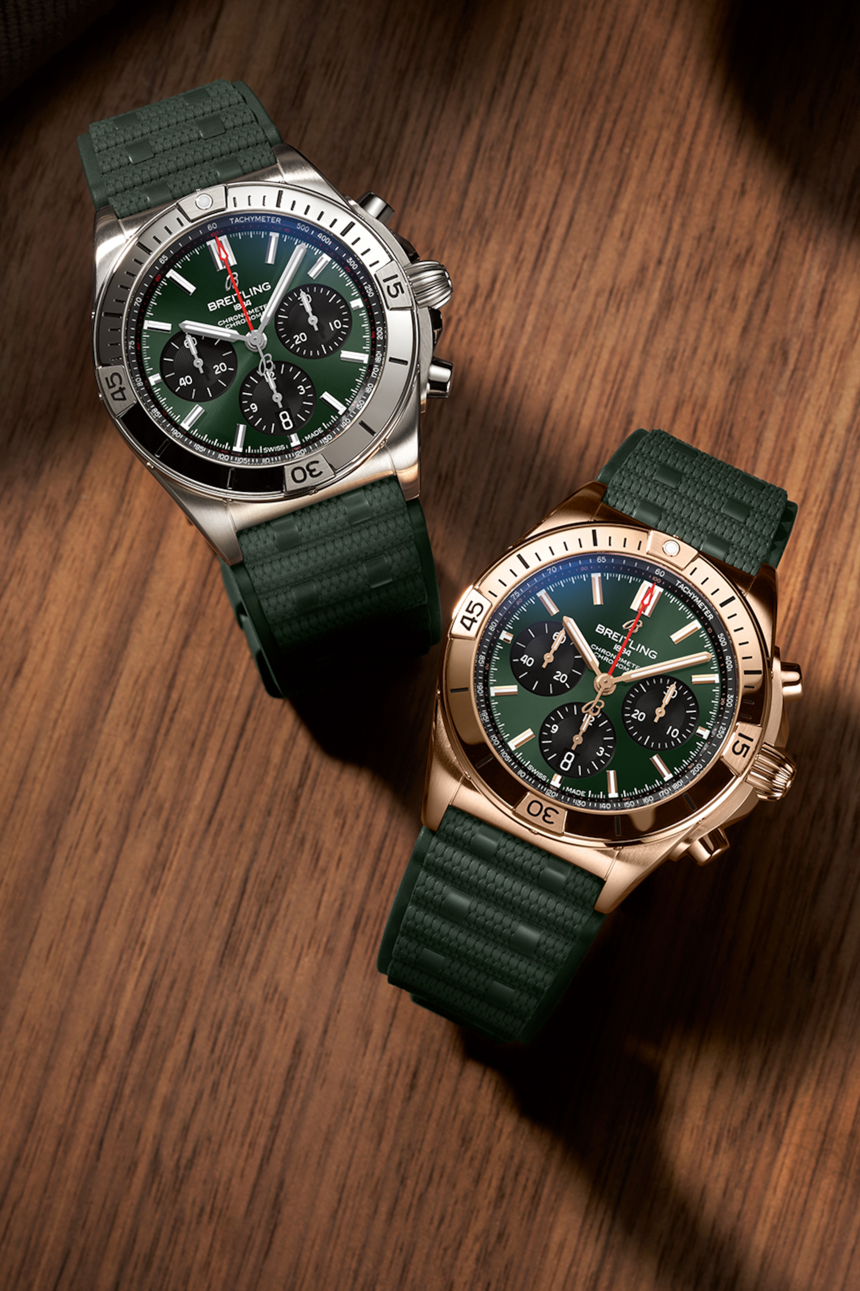 一金一銀的 Chronomat，搭配深綠色橡膠錶帶，放在棕色桌子上。